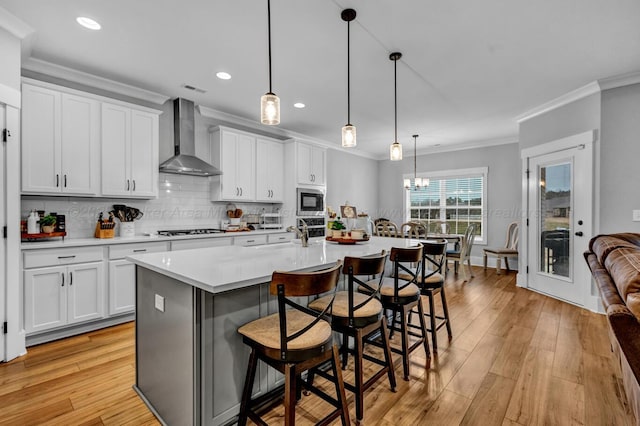 kitchen with appliances with stainless steel finishes, white cabinets, a kitchen bar, a center island with sink, and wall chimney exhaust hood