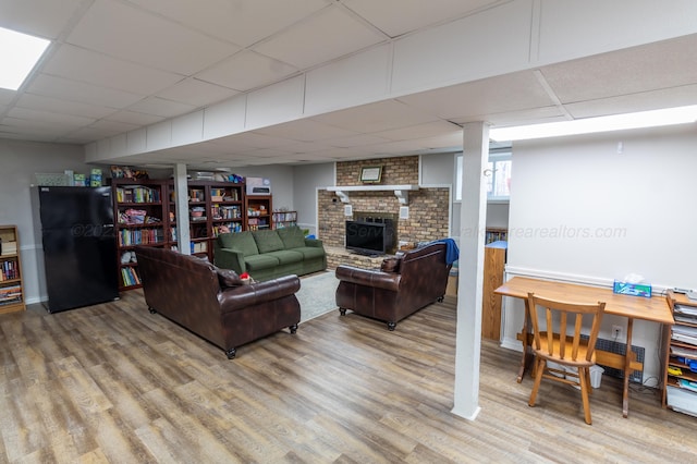 living area featuring a drop ceiling, wood finished floors, and a brick fireplace