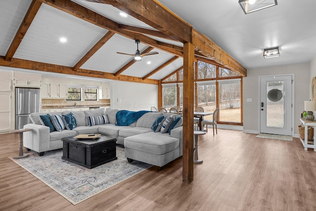 living area with vaulted ceiling with beams, a ceiling fan, baseboards, and light wood finished floors