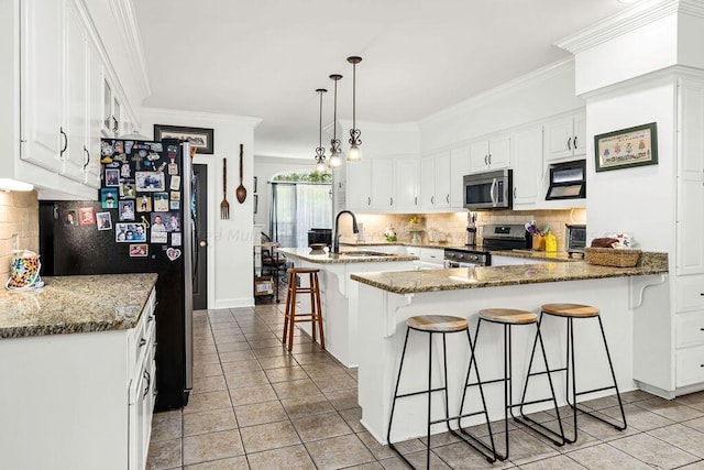 kitchen with a kitchen bar, appliances with stainless steel finishes, dark stone counters, sink, and decorative light fixtures