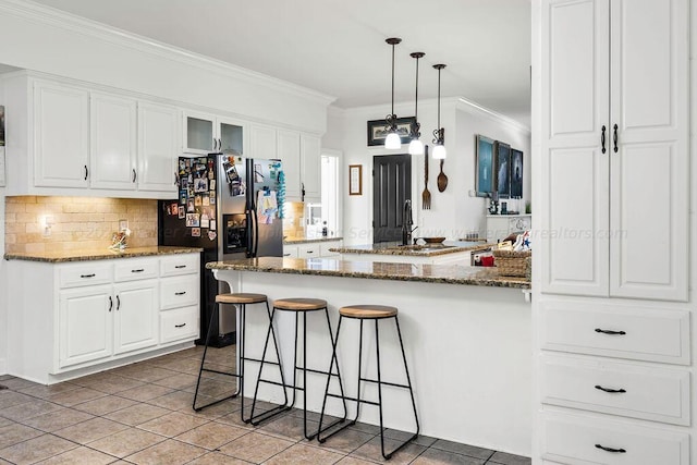 kitchen featuring white cabinetry, a kitchen breakfast bar, stainless steel refrigerator with ice dispenser, dark stone countertops, and decorative light fixtures