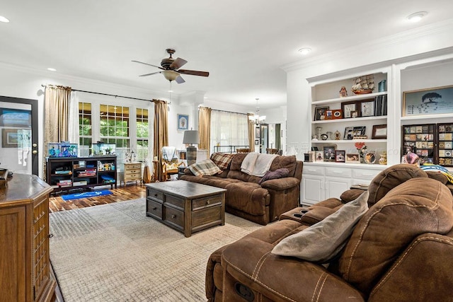 living room featuring built in features, ornamental molding, ceiling fan with notable chandelier, and light wood-type flooring