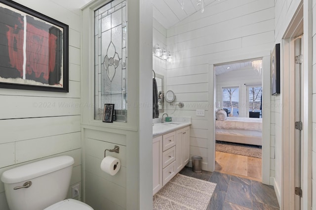 ensuite bathroom with lofted ceiling, toilet, wood walls, vanity, and ensuite bath