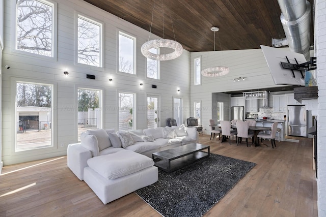 living area with wooden ceiling, light wood finished floors, a towering ceiling, and wood walls