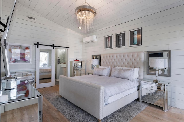 bedroom featuring lofted ceiling, visible vents, light wood-style flooring, a barn door, and an AC wall unit