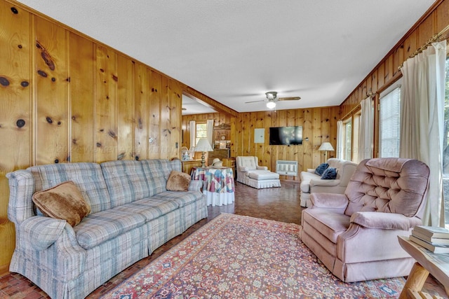 living room featuring wooden walls, ceiling fan, and a textured ceiling