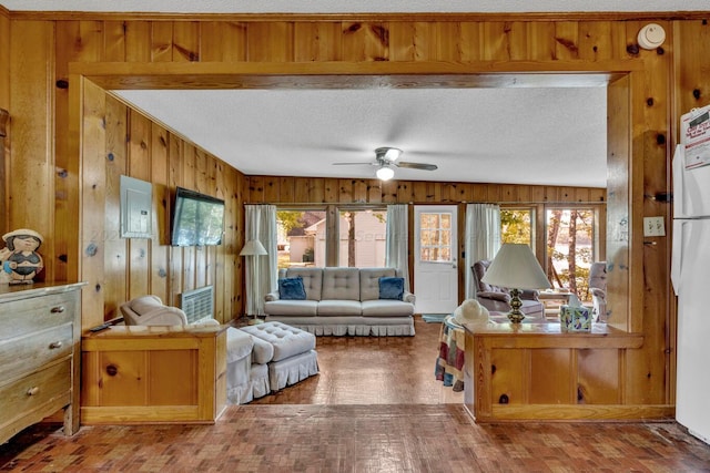 interior space with ceiling fan, wood walls, a textured ceiling, and electric panel