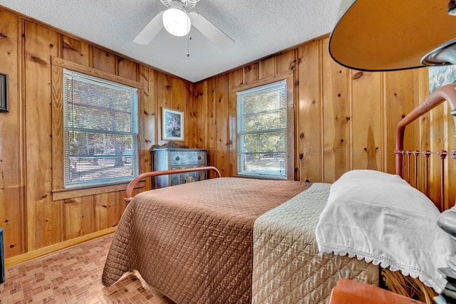 bedroom featuring a textured ceiling, ceiling fan, and wooden walls