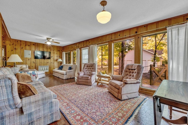 living room with a textured ceiling, hardwood / wood-style flooring, ceiling fan, and wood walls