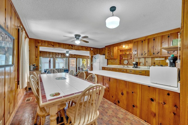 dining space with ceiling fan, wood walls, and a textured ceiling