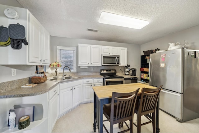 kitchen with stainless steel appliances, white cabinetry, sink, and a textured ceiling