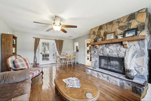 living room featuring a fireplace, wood-type flooring, a textured ceiling, and ceiling fan