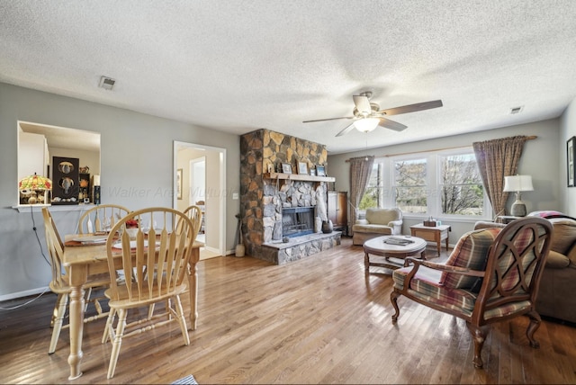 living room with wood-type flooring, a textured ceiling, ceiling fan, and a fireplace