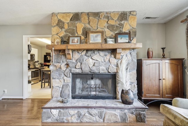 interior details with stainless steel appliances, a stone fireplace, wood-type flooring, and a textured ceiling