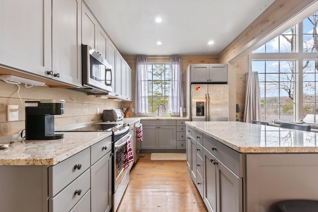 kitchen featuring gray cabinetry, light stone counters, stainless steel appliances, and light hardwood / wood-style floors