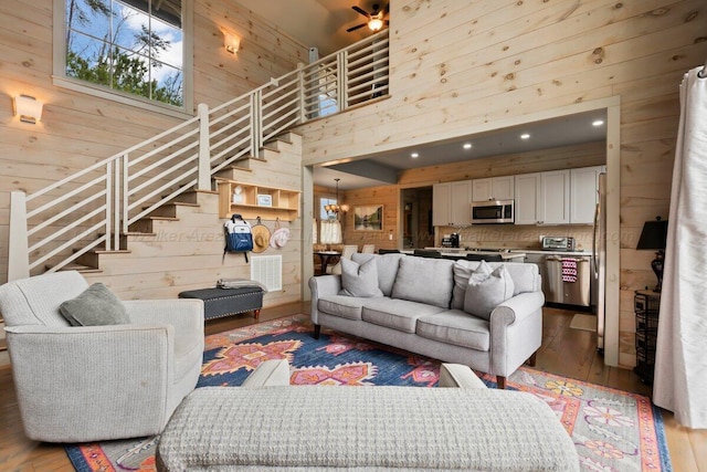 living room featuring hardwood / wood-style flooring, wooden walls, an inviting chandelier, and a high ceiling