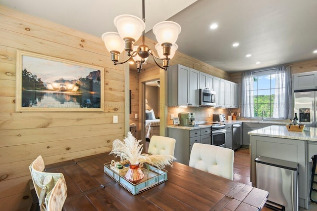 dining room featuring dark hardwood / wood-style flooring, sink, wooden walls, and a chandelier