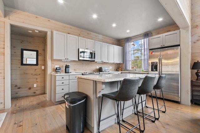 kitchen with white cabinetry, wooden walls, a kitchen breakfast bar, stainless steel appliances, and a center island