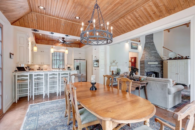 dining room with ceiling fan with notable chandelier, a fireplace, sink, a high ceiling, and wood ceiling