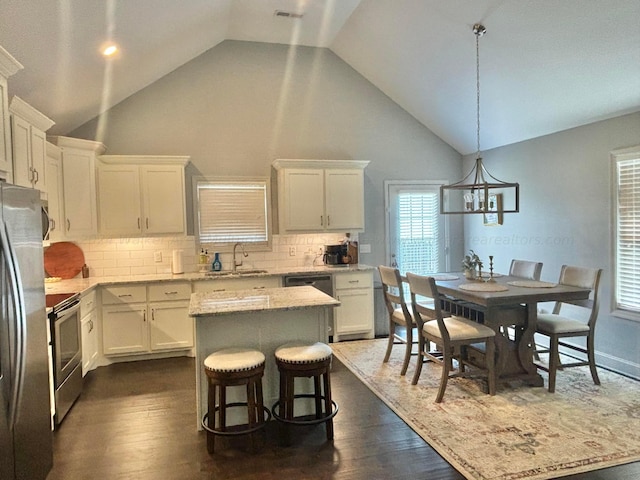 kitchen with appliances with stainless steel finishes, pendant lighting, white cabinets, a center island, and dark hardwood / wood-style floors