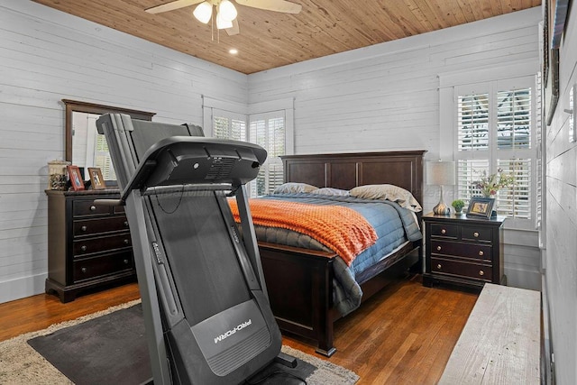 bedroom with a ceiling fan, wooden walls, wooden ceiling, and dark wood finished floors