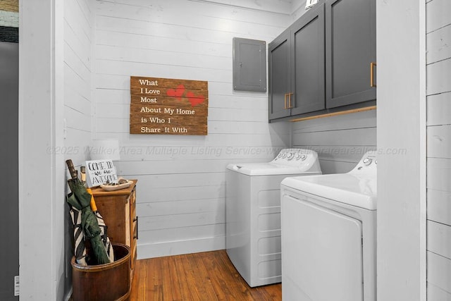 laundry room with washing machine and clothes dryer, dark wood-style floors, cabinet space, and wooden walls