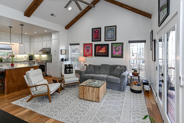 living room with beam ceiling, high vaulted ceiling, light hardwood / wood-style flooring, and ceiling fan