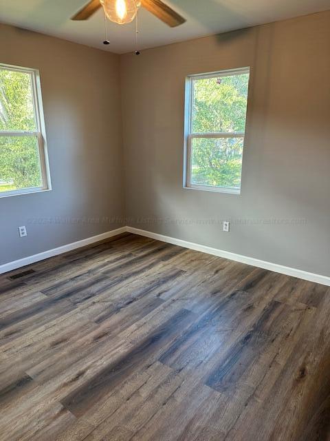 empty room with dark wood-type flooring, ceiling fan, and a healthy amount of sunlight