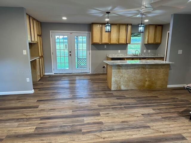 kitchen with pendant lighting, dark wood-type flooring, french doors, sink, and light stone counters