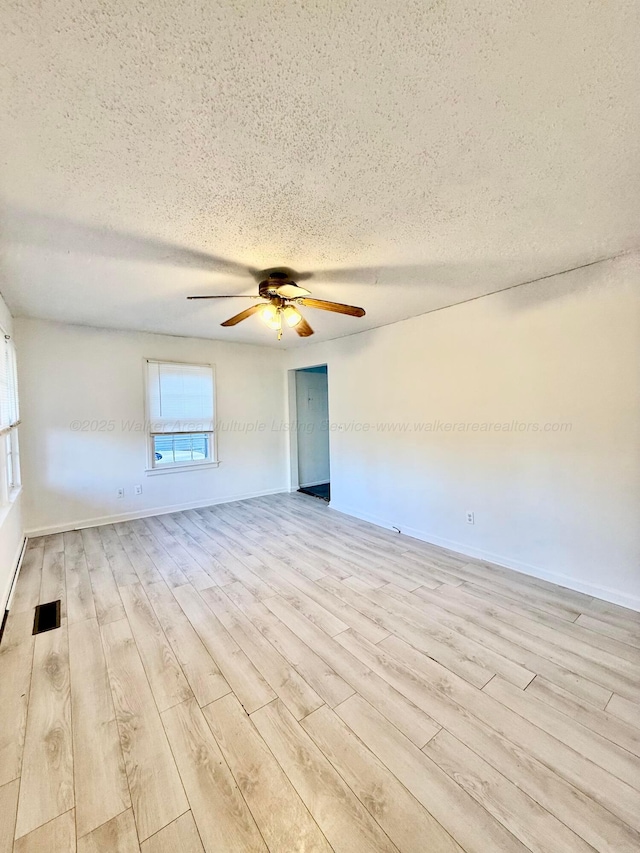 empty room with visible vents, a ceiling fan, a textured ceiling, wood finished floors, and baseboards