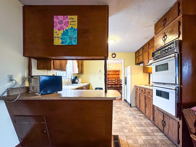 kitchen featuring sink, white double oven, fridge with ice dispenser, a textured ceiling, and kitchen peninsula