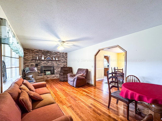 living room featuring a fireplace, wood-type flooring, a textured ceiling, and ceiling fan