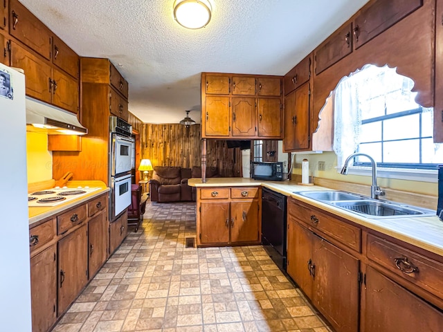 kitchen with sink, a textured ceiling, wooden walls, kitchen peninsula, and black appliances