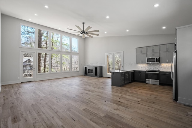 unfurnished living room featuring hardwood / wood-style flooring, high vaulted ceiling, ceiling fan, and sink