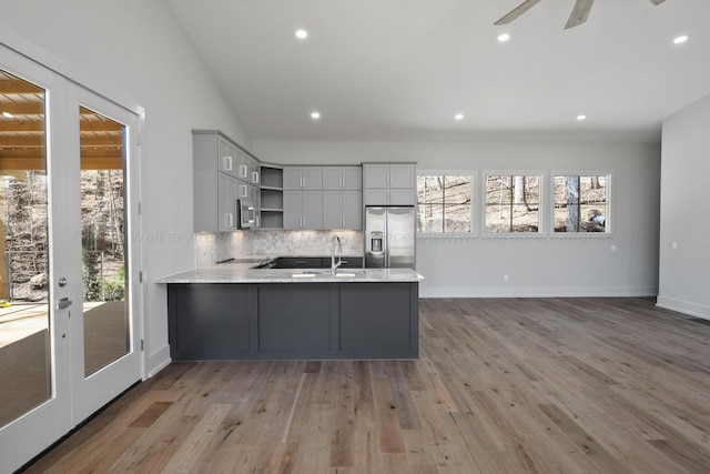 kitchen featuring kitchen peninsula, decorative backsplash, stainless steel appliances, light hardwood / wood-style flooring, and lofted ceiling