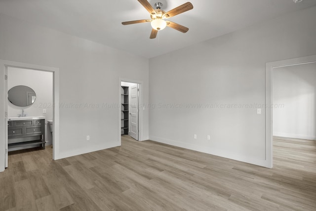 interior space with ceiling fan, sink, a spacious closet, ensuite bathroom, and light wood-type flooring