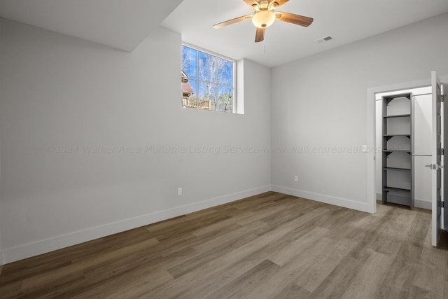 unfurnished bedroom with ceiling fan, a closet, a spacious closet, and light wood-type flooring