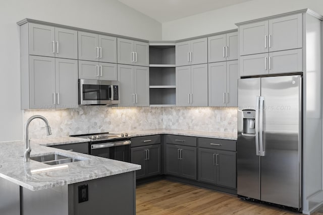 kitchen with sink, light stone counters, kitchen peninsula, decorative backsplash, and appliances with stainless steel finishes