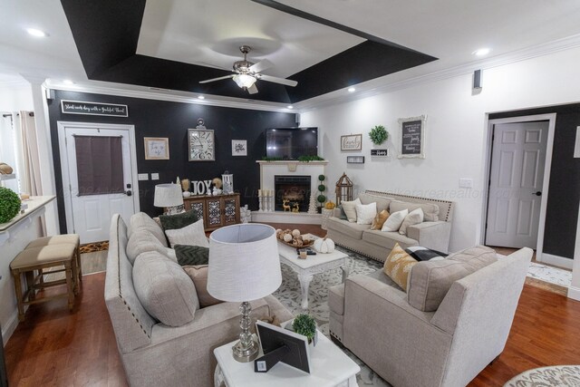 living room with a tray ceiling, ceiling fan, dark hardwood / wood-style flooring, and crown molding