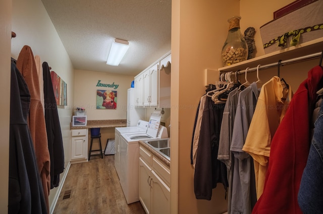 laundry area with cabinets, washing machine and clothes dryer, light hardwood / wood-style floors, and a textured ceiling