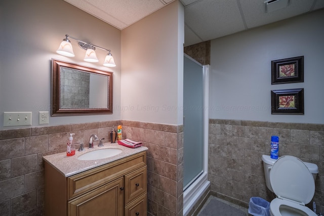 bathroom with a paneled ceiling, tile walls, vanity, an enclosed shower, and toilet