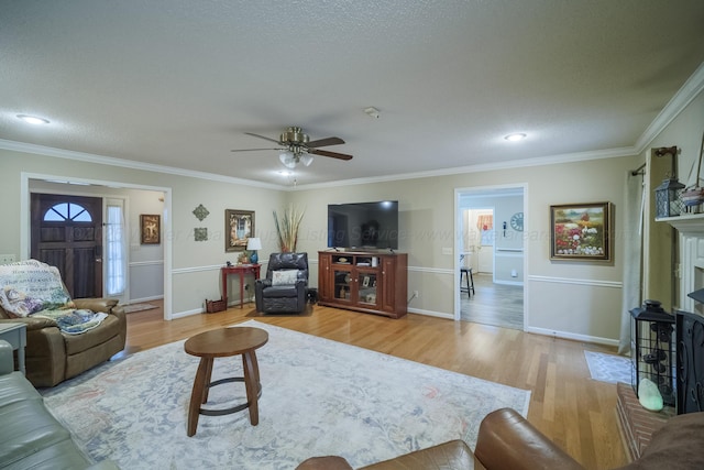 living room with crown molding, light hardwood / wood-style flooring, ceiling fan, a textured ceiling, and a brick fireplace