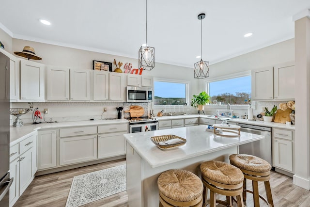 kitchen with pendant lighting, appliances with stainless steel finishes, a kitchen island, white cabinets, and a kitchen bar