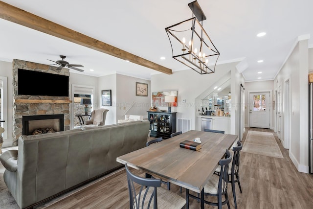 dining room featuring a fireplace, beam ceiling, light hardwood / wood-style flooring, and ornamental molding