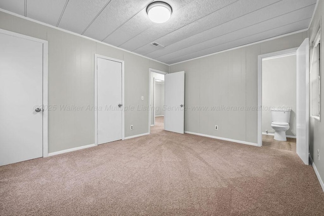 unfurnished bedroom with a textured ceiling, connected bathroom, carpet floors, and ornamental molding