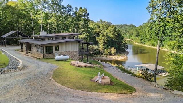 view of front of house featuring a water view, stone siding, driveway, and a view of trees