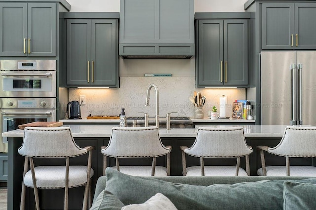 kitchen with tasteful backsplash, appliances with stainless steel finishes, light countertops, a kitchen bar, and a sink