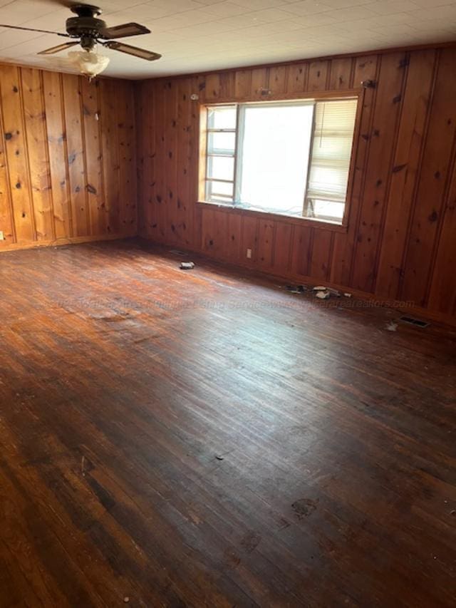 unfurnished room with dark wood-type flooring, ceiling fan, and wood walls