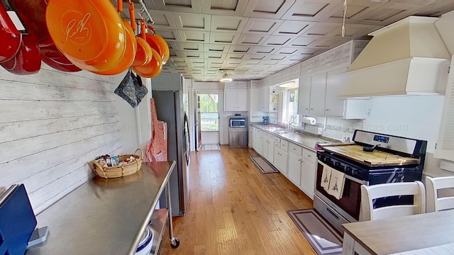 kitchen featuring ventilation hood, stainless steel appliances, sink, light hardwood / wood-style flooring, and white cabinets