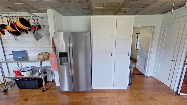 kitchen featuring white cabinetry, wooden walls, wood-type flooring, and stainless steel refrigerator with ice dispenser